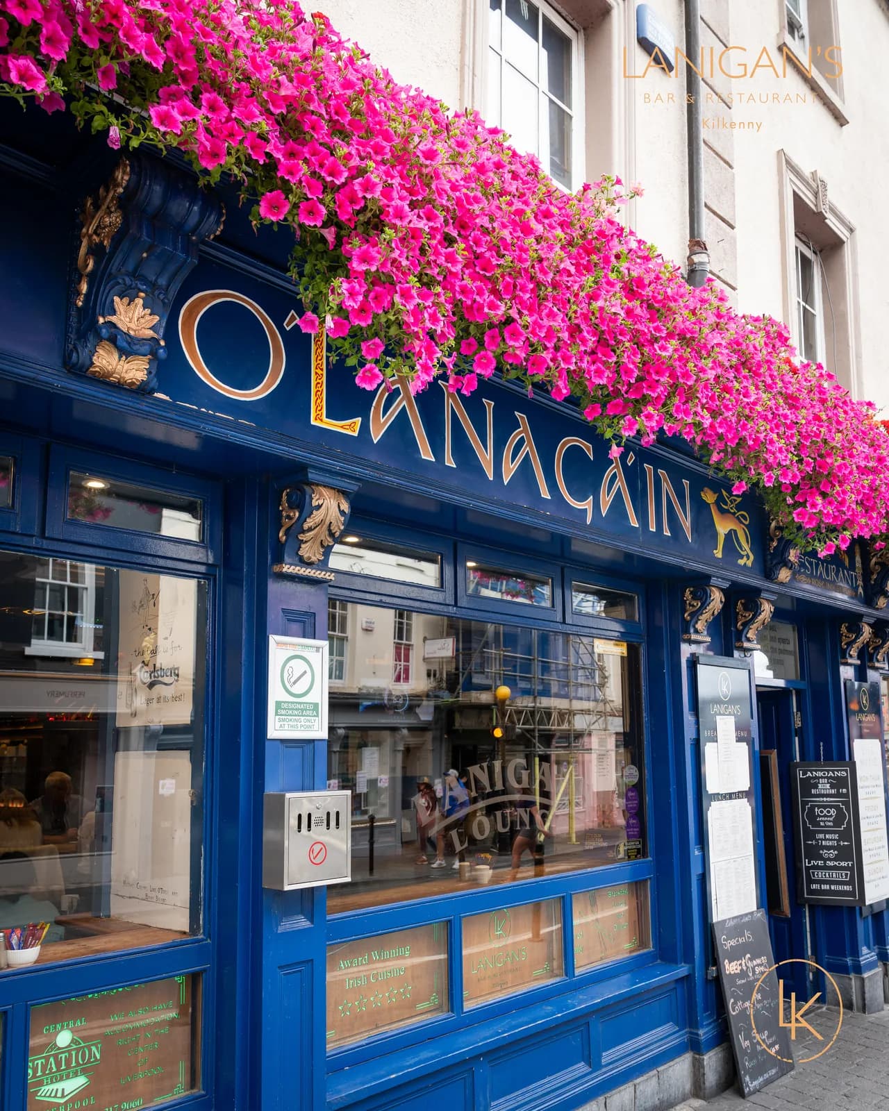 Gold Ó Lanagáin lettering and pink flower display on the blue frontage of Lanigan's Bar, Rose Inn Street, Kilkenny